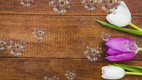 Animation-of-floating-floral-heart-shapes-over-tulips-on-wood-background