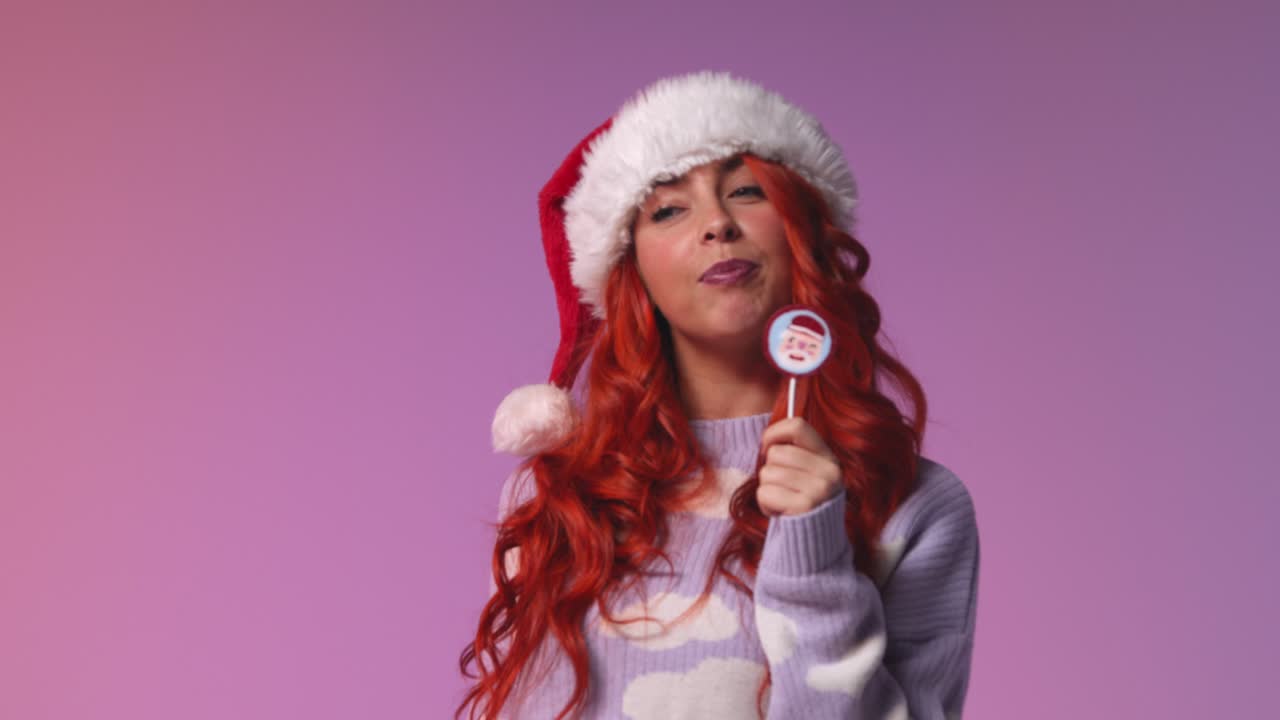 retrato de estudio de una mujer joven de la generación z con sombrero de papá noel lamiendo caramelos y piruletas