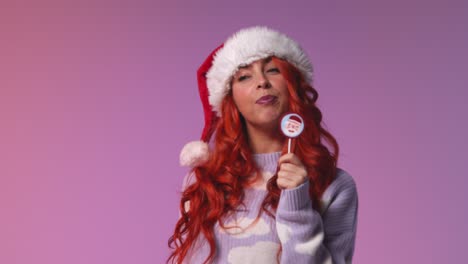 retrato de estudio de una mujer joven de la generación z con sombrero de papá noel lamiendo caramelos y piruletas