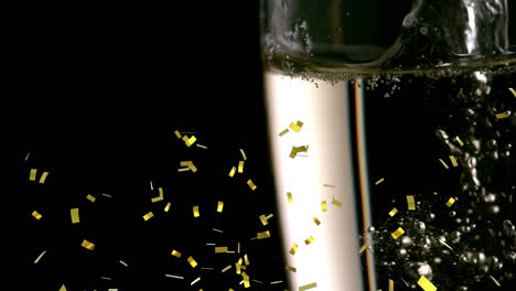 golden confetti falling over close up of champagne bubbles in a glass against black background