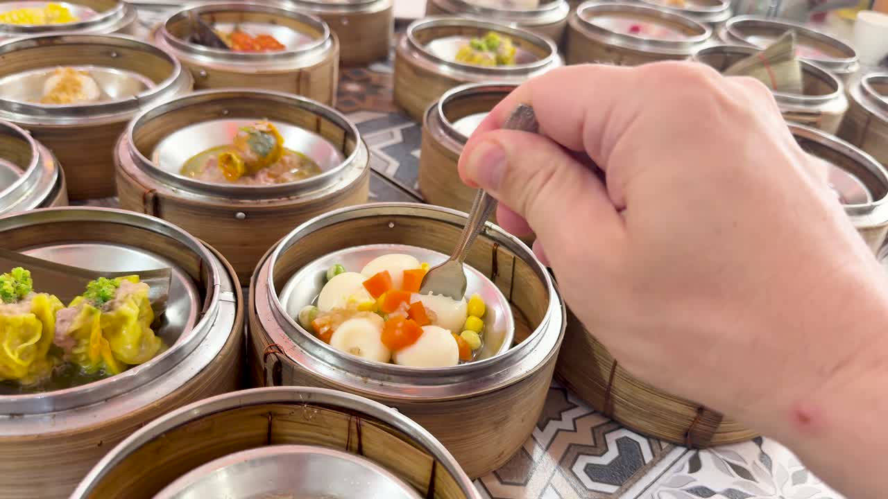 Hand picks dim sum with fork from bamboo baskets under bright natural lighting, close-up view