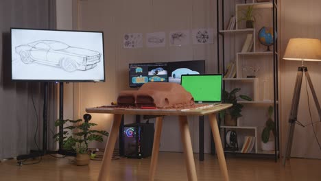 the sculpture of car clay beside green screen laptop is on the table in the studio with tv and computers display 3d electric car model