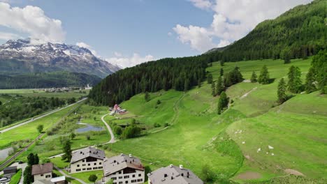 aerial flying over town of samedan towards green hillside covered with forest trees on sunny clear day