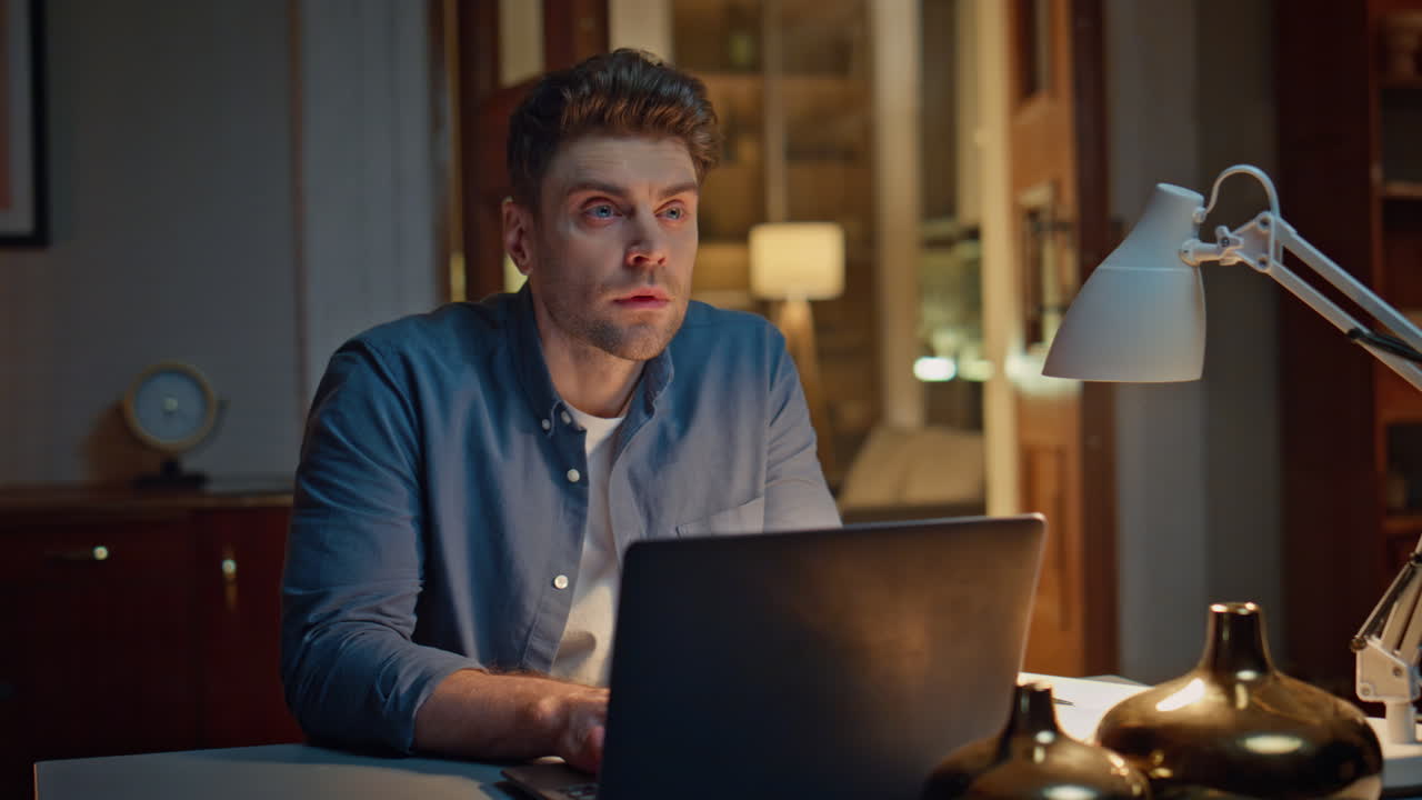 Focused guy browsing internet on pc at dark home closeup. Man typing laptop