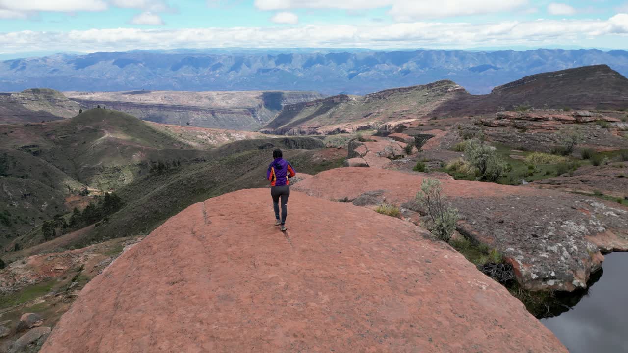Sorvolo: Donna cammina verso un punto panoramico su una scarpata di arenaria in Bolivia.