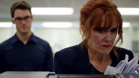 a woman in a professional outfit struggles with a paper jam at an office printer while colleagues look on. the atmosphere is tense as they navigate office chaos and deadlines.