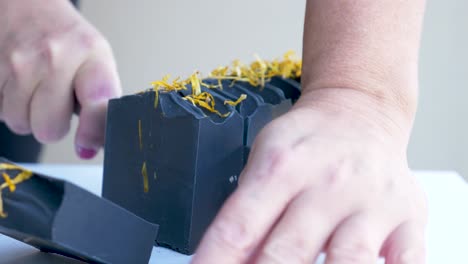 A-women-gently-slices-a-newly-made-block-of-black-handmade-soap-with-a-sharp-knife