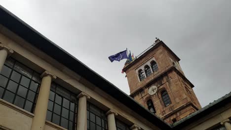 clock tower on oviedo's university building with waving flags on a cloudy day, seen in oviedo's city center