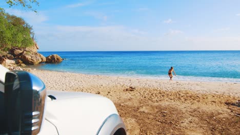 Frau-Im-Bikini-Sitzt-Am-Strand-Mit-Einem-Auto-Im-Vordergrund