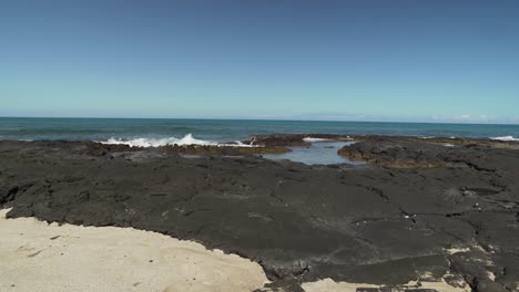 waves hitting black lava rock formations on a hawaiian island