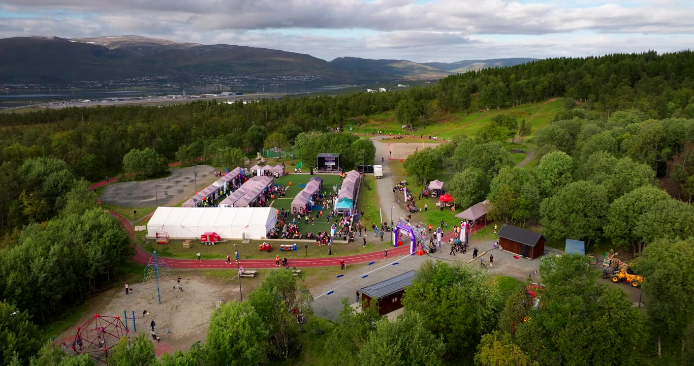 Valkoisia telttoja, juoksurata ja ihmisiä kokoontumassa ulkona järjestettävään Relay for Life -tapahtumaan Tromssassa, Norjassa. Ilmakuva dronella.