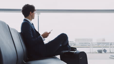 pull focus shot of businessman sitting in airport departure lounge using mobile phone