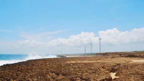 wind turbines spinning along rocky beach with ocean waves in curacao, caribbean