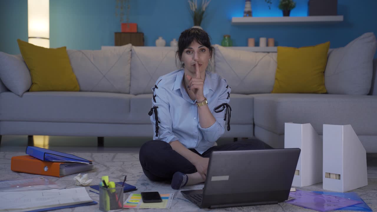 una mujer que trabaja en una oficina en casa dice "shhh" a la cámara.