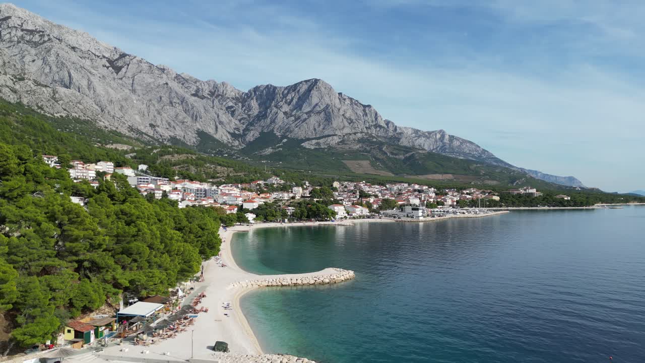 Lenta ripresa aerea con drone sopra la spiaggia di Brela, Croazia, in una giornata calma con nuvole leggere e cielo blu