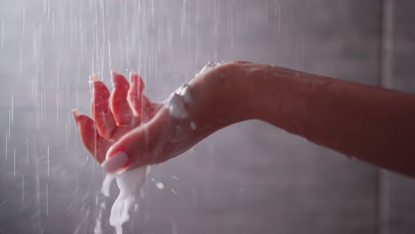 woman holds foamy palm under shower sprays closeup. lady washes body with skin moisturizing mouse for spa procedures in bathroom. skincare cosmetic