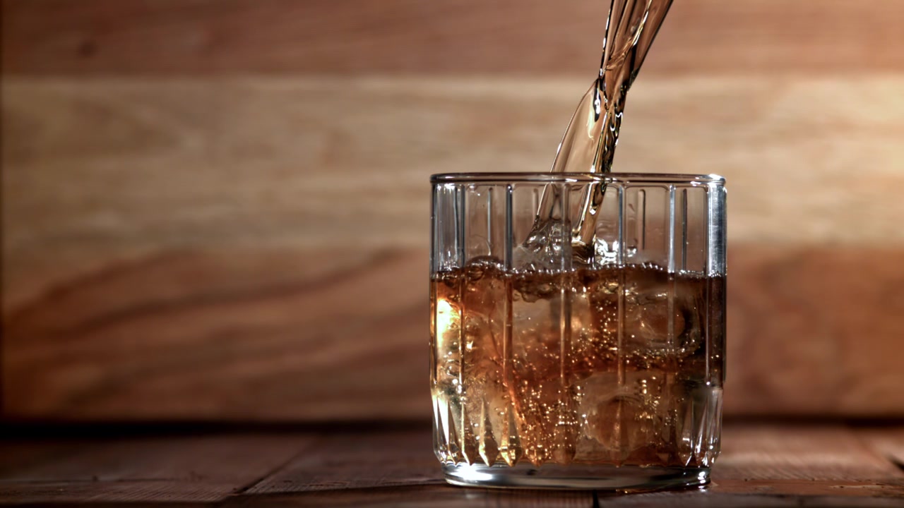 Whisky dorato versato su ghiaccio in un bicchiere tumbler
