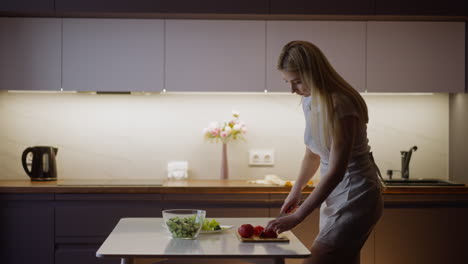 woman cuts ripe red tomato to make tasty salad at table