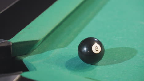 up shot of black billiard ball rolling towards pool pocket after being hit by white cue ball on green pool table. close-up captures precision, motion, and dynamics of gameplay in billiards