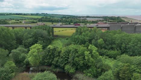 lush greenery and a flowing waterway in the foreground with a large industrial structure behind