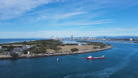 large industrial ship positioned in a coastal ocean inlet with a urban skyline in the distance