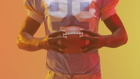 Video-of-midsection-of-african-american-american-football-player-with-ball-over-orange-background