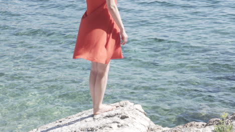 Woman-standing-on-a-cliff-at-the-sea,-wind-blowing-her-skirt