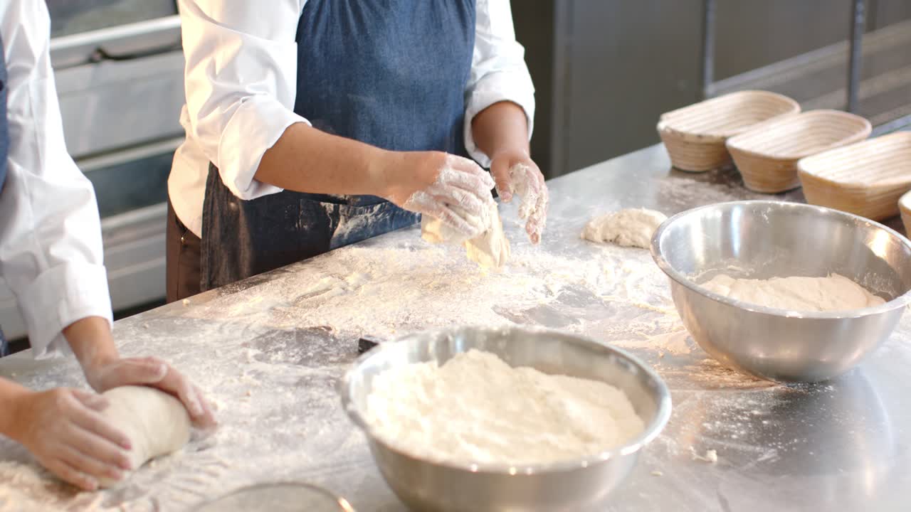 Diverse female bakers scooping flour, shaping and folding dough at counter, preparing for proofing