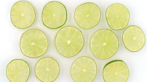 On-a-white-background-sliced-pieces-of-lime-are-sprinkled-with-water.-Juicy-fresh-lime-in-slow-motion.-Lots-of-lime-slices.