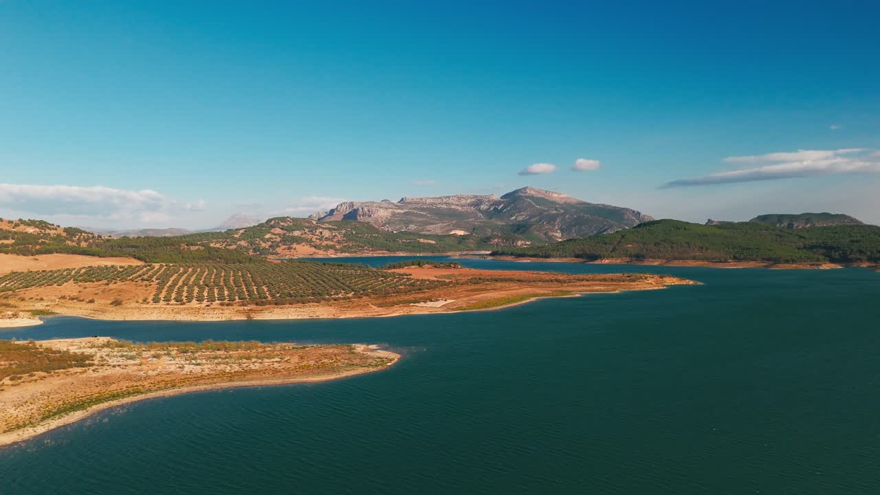Costa del lago con cime distanti sotto un cielo sereno