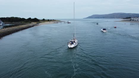 aerial view following behind luxury sailboat travelling along scenic river estuary