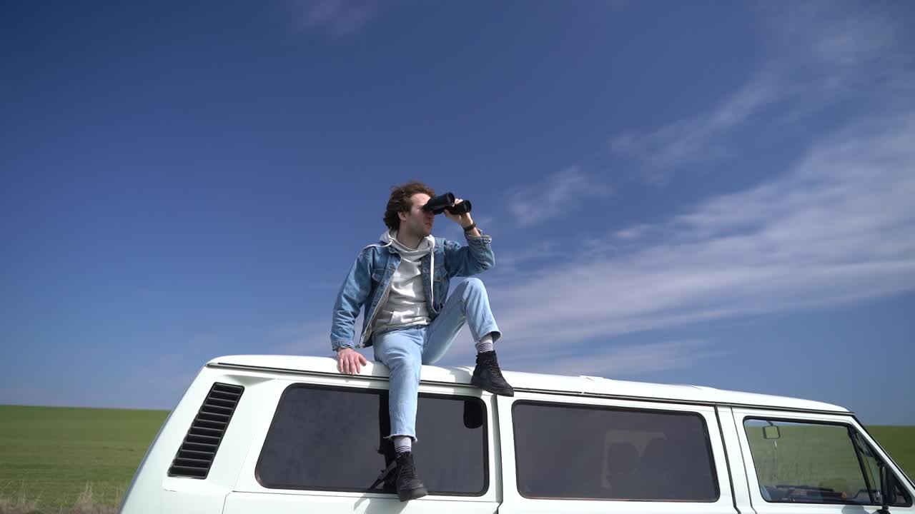 un niño mira a su alrededor con un par de binoculares en el techo de una caravana.