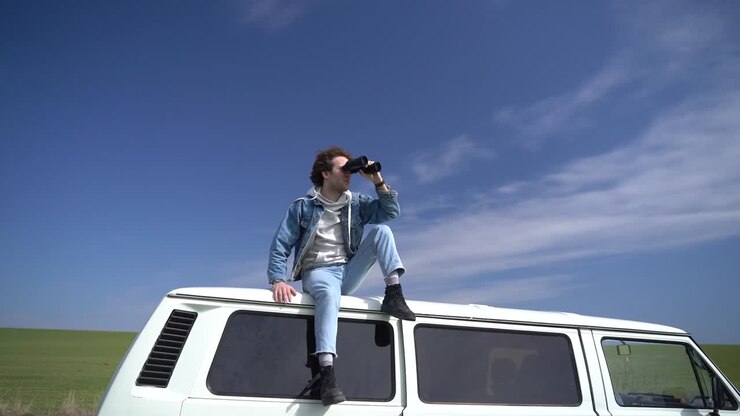 Ein junger Junge schaut sich mit einem Fernglas auf dem Dach eines Wohnwagens um.