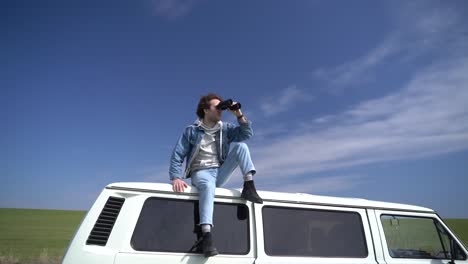 young boy looks around with a pair of binoculars on the roof of a caravan.