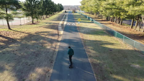 An-aerial-tracking-of-a-man-on-an-electric-skateboard-in-an-empty-park-on-a-sunny-day