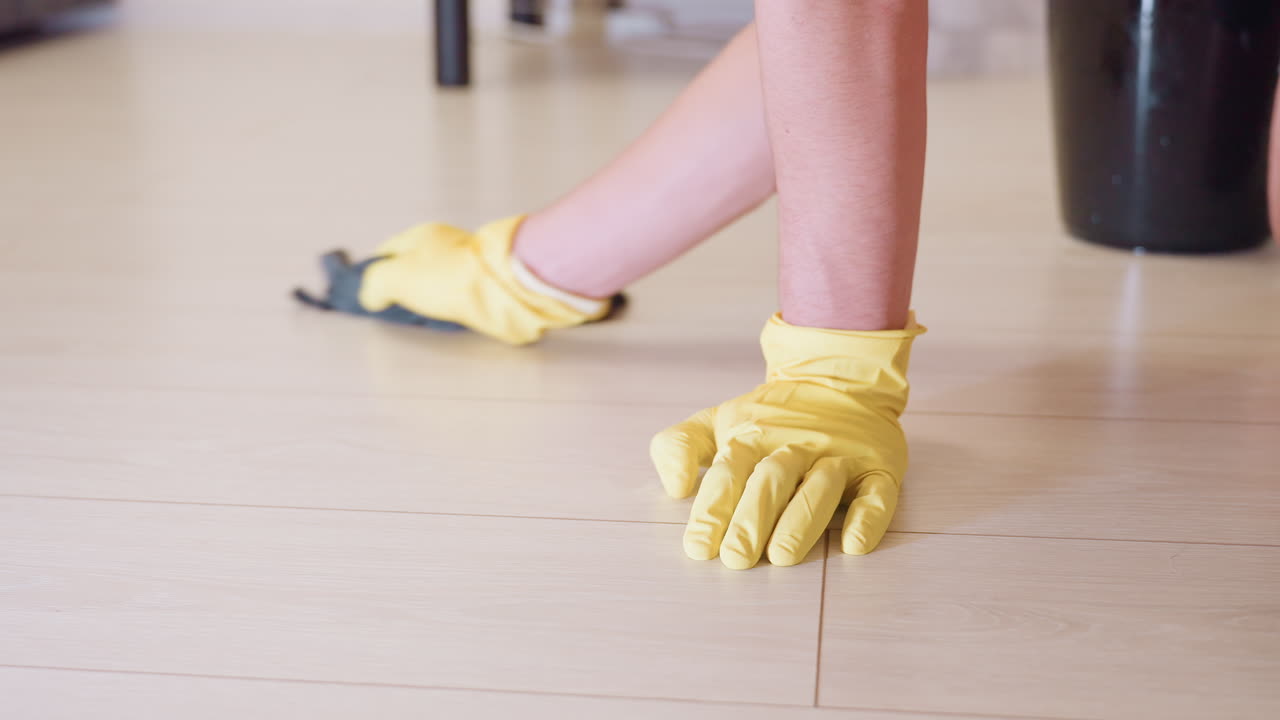 House keeper in yellow gloves kneeling down scrubbing wooden floor with cloth, focusing on cleanliness, hygiene, and domestic care while maintaining sanitation