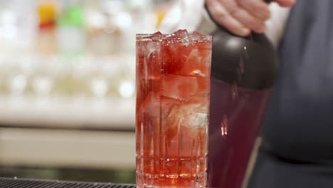 bartender pouring red alcohol into a mixed drink at a bar