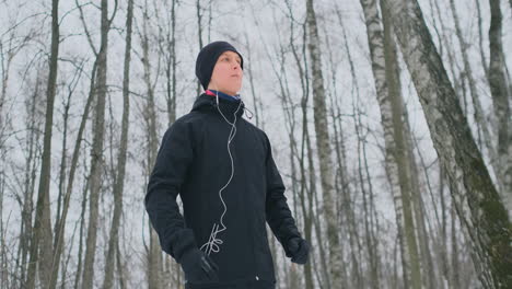 un joven que corre por la mañana sostiene auriculares en sus manos y se los inserta en los oídos antes de correr en el parque. carrera de invierno. utilice dispositivos y aplicaciones de formación modernos. escuchar música mientras entrenas mientras corres
