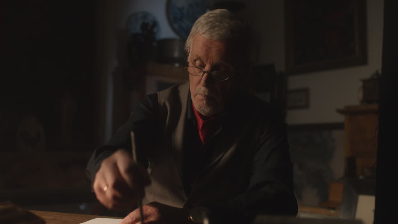 Old passionate man writes a letter in his office at night