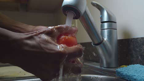 black man open faucet and rinse red tomato in the sink - medium shot