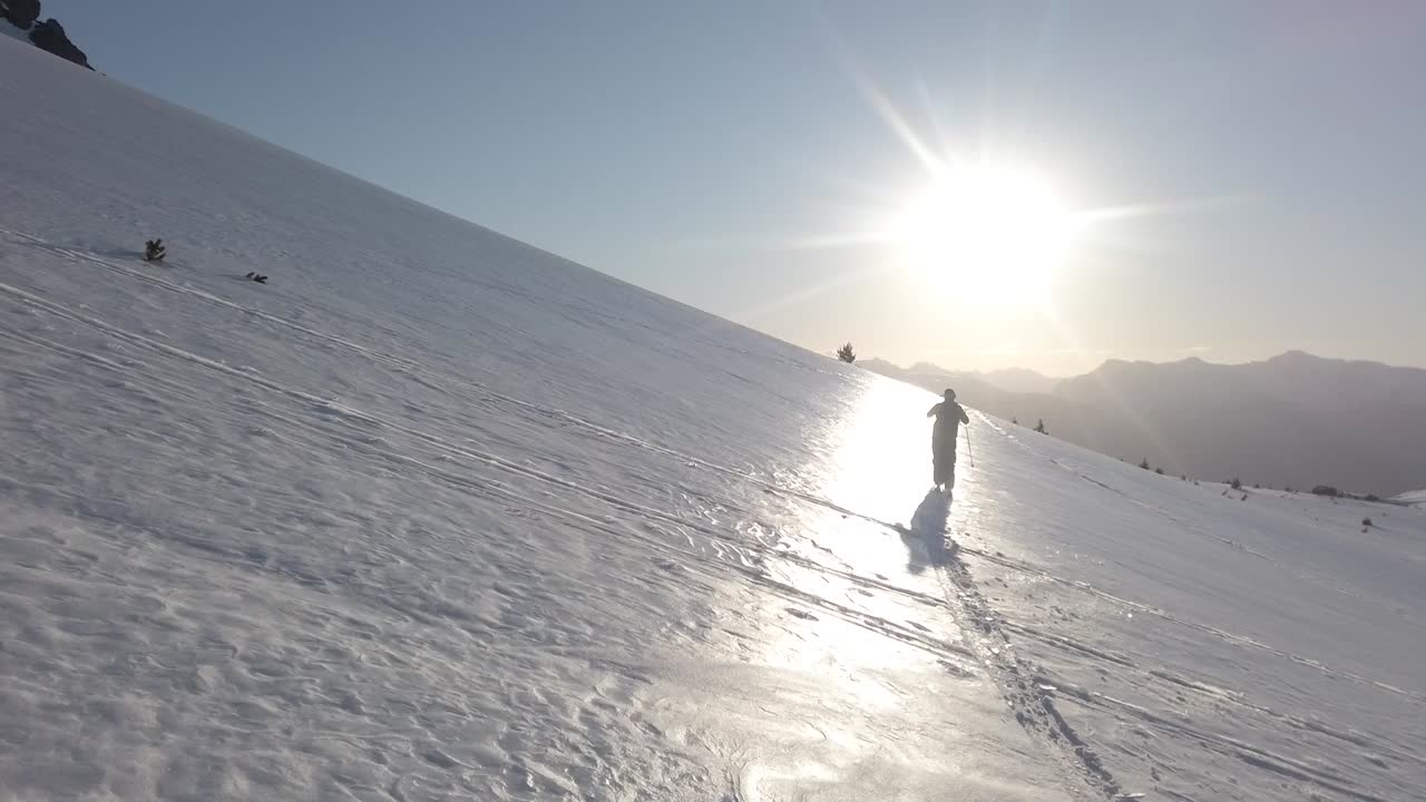 Dolly in following a man skiing alone across snow covered Piltriquitron Hill at sunset, El Bolsón, Patagonia Argentina