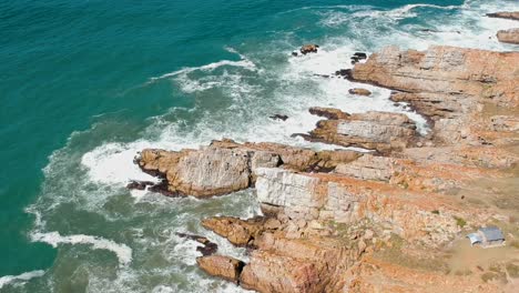 Drone-view-of-orange-rocky-coast-with-blue-teal-waves