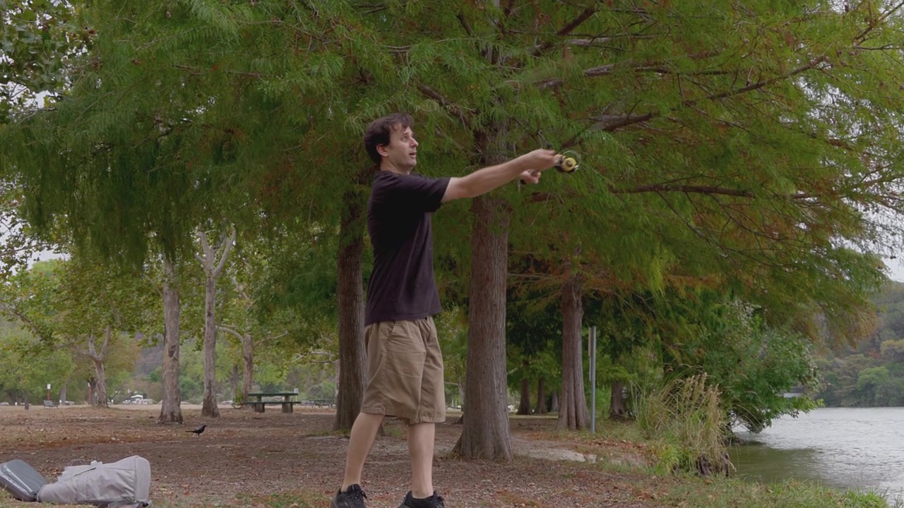 A young man casts his fishing line into the lake, showcasing his outstretched arm and focus on the serene water.
