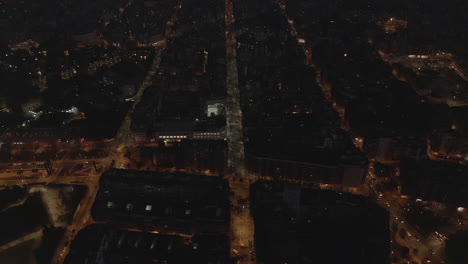 Vista-Aérea-De-La-Ciudad-Por-La-Noche.-Calles-Y-Edificios-Iluminados-En-El-Barrio-Urbano-Desde-La-Altura.-Barcelona,-España