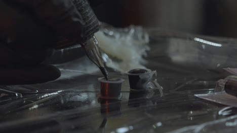 a tattoo artist dips the tip of the tatto pen or iron into ink to load the gun on a sterile tray for tattooing