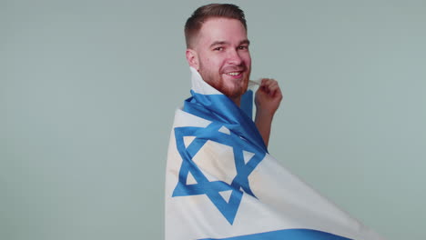 Man-waving-and-wrapping-in-Israel-national-flag,-celebrating-Independence-day-on-gray-background