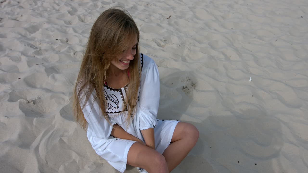 Happy smiling girl sitting on sand on the beach.