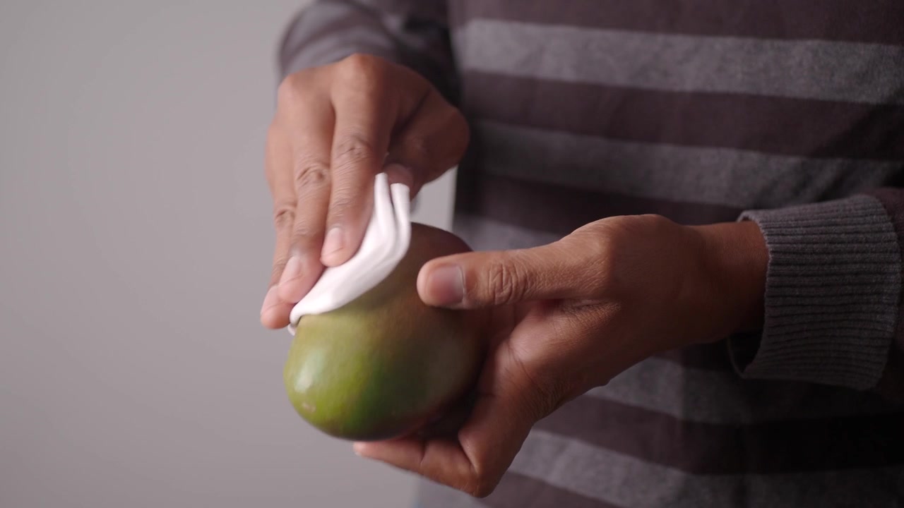 Primer plano de manos limpiando un mango fresco con un paño