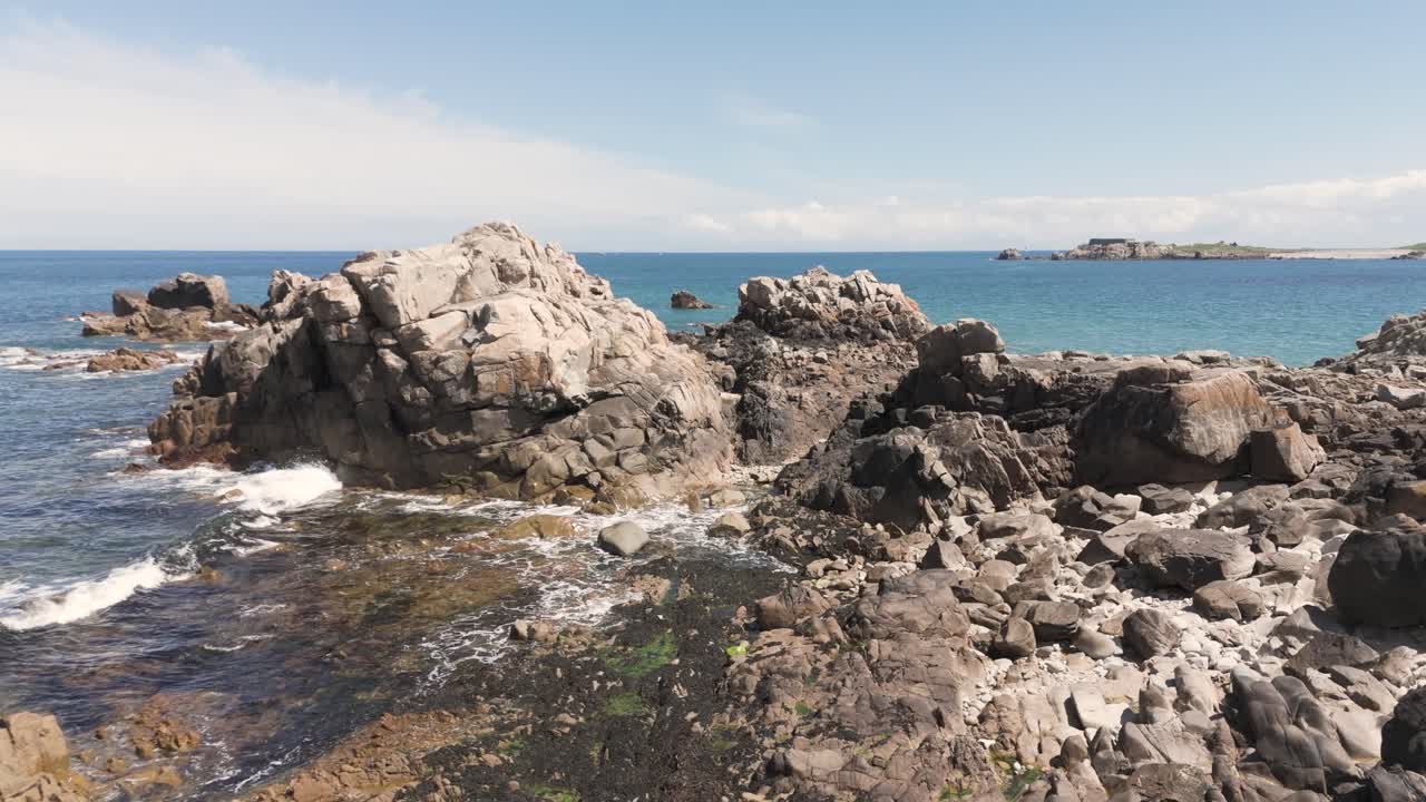 las olas se lavan suavemente en la ensenada en la costa rocosa en un brillante día soleado en guernsey con vistas a un cabo lejano