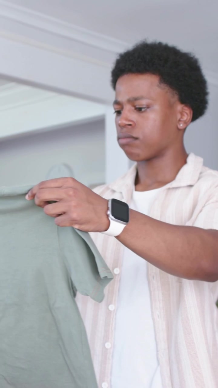 Vertical video: Lifting green t-shirt, adult male wearing striped overshirt inspecting fit at home